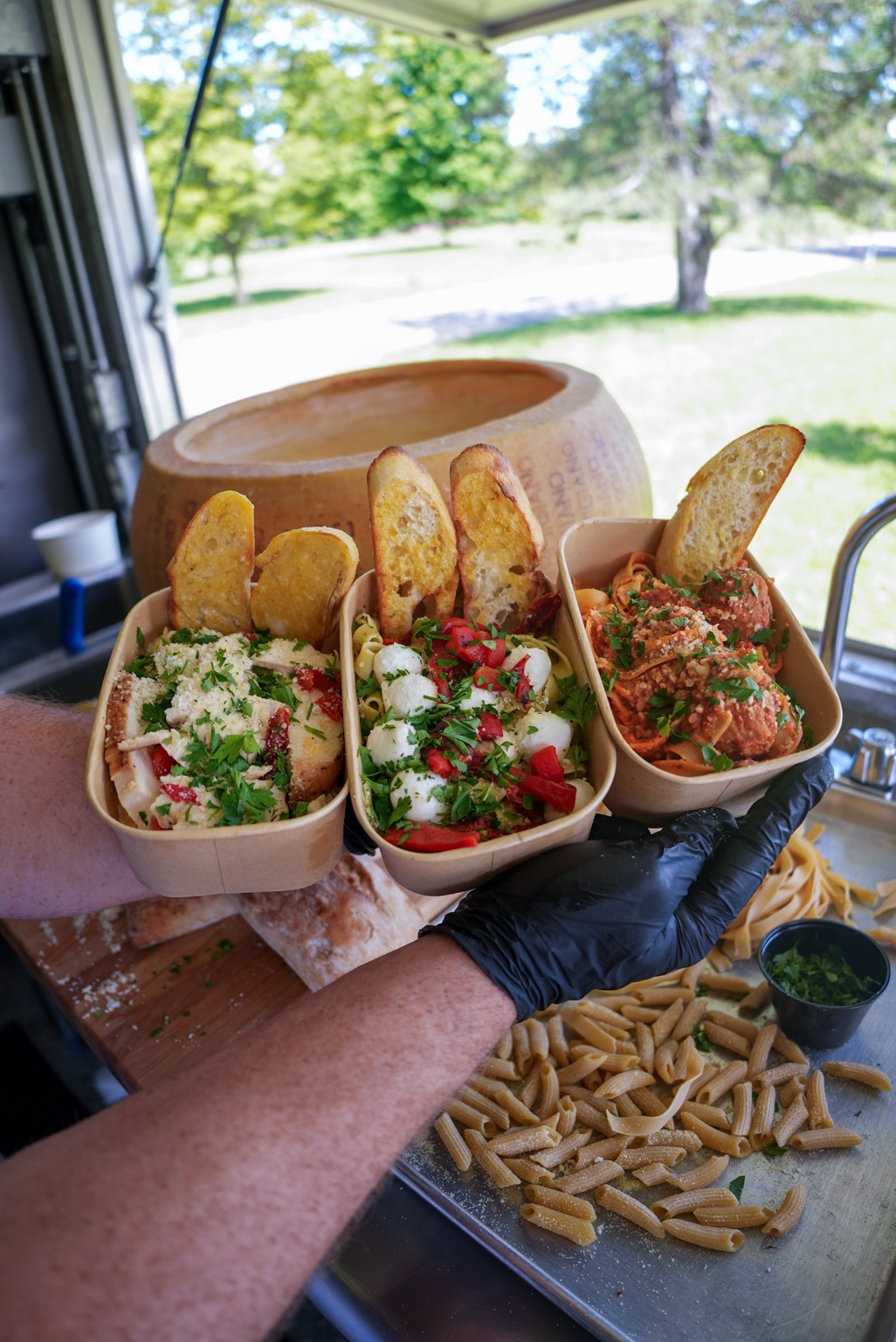Three fresh pasta bowls presented beside the cheese wheel
